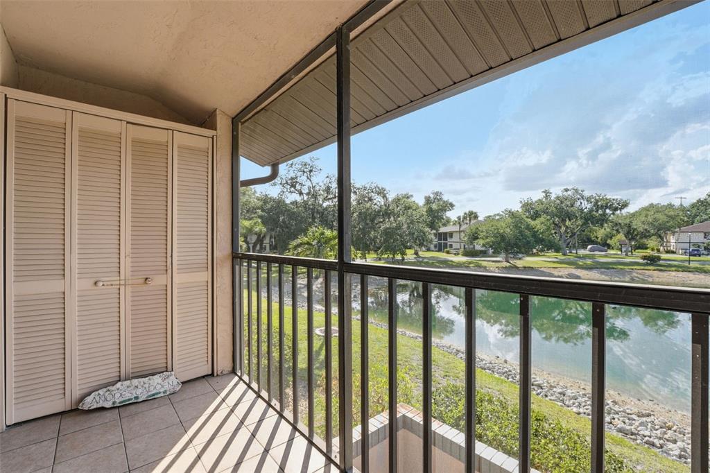 A screened-in balcony with tile flooring overlooks a pond and green space — 19505 QUESADA AVENUE UNIT AA204, PORT CHARLOTTE, FL