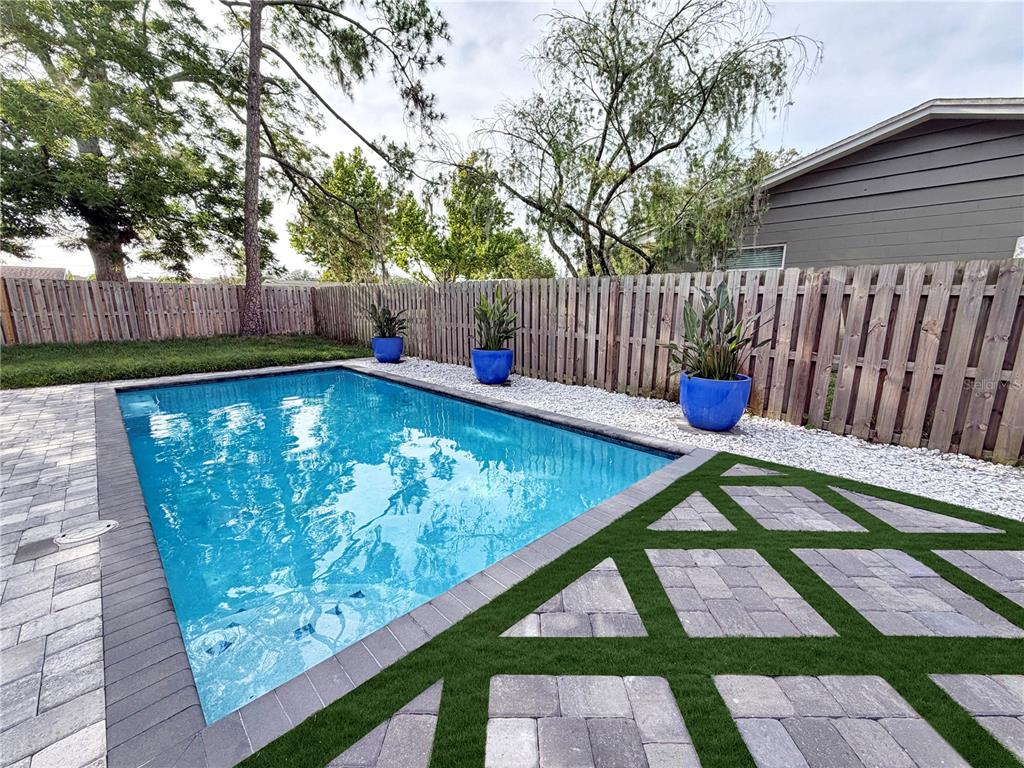 A rectangular swimming pool sits beside a paver patio with artificial turf and blue planters — 20 E DIVISION STREET, WINTER GARDEN, FL