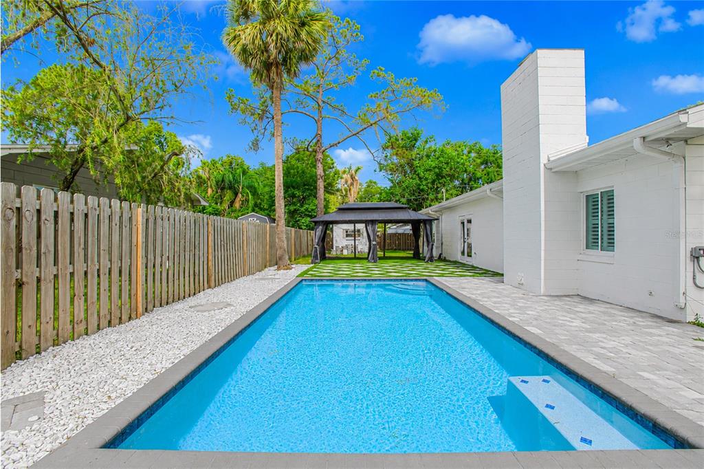 A rectangular swimming pool sits in a backyard next to a white house and gazebo — 20 E DIVISION STREET, WINTER GARDEN, FL