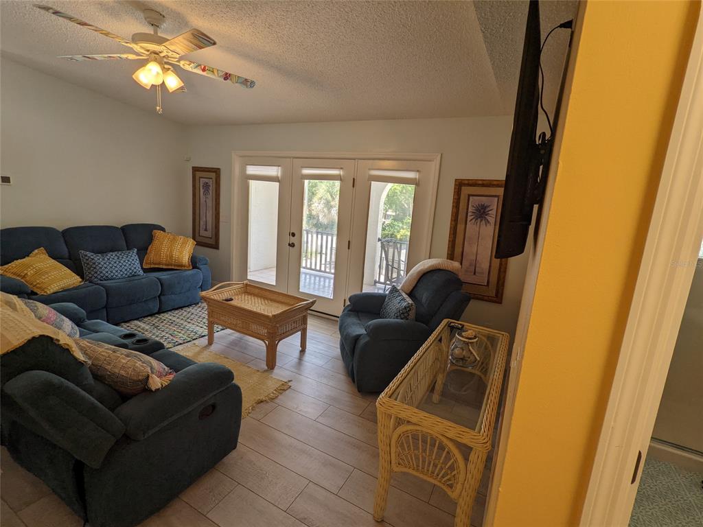 A living room features blue sofas, a wicker coffee table, and glass doors to a balcony — 203 CANOVA DRIVE, NEW SMYRNA BEACH, FL