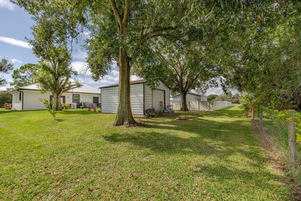 A grassy backyard features a metal shed, mature trees, and a white house — 1014 SW 11th Street, Okeechobee FL 34974, OKEECHOBEE, FL