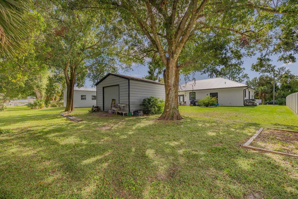 A backyard features a metal shed, large shade trees, and a white house with siding — 1014 SW 11th Street, Okeechobee FL 34974, OKEECHOBEE, FL
