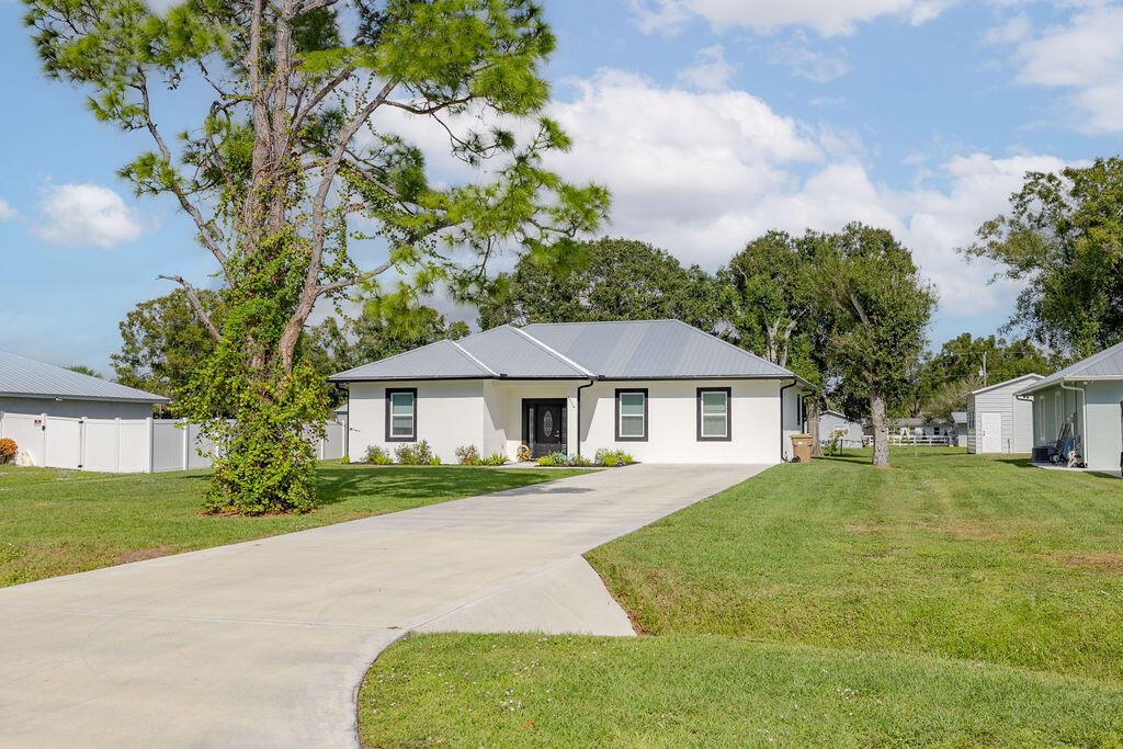 A white single-story house with a metal roof and a concrete driveway sits on grass — 1014 SW 11th Street, Okeechobee FL 34974, OKEECHOBEE, FL