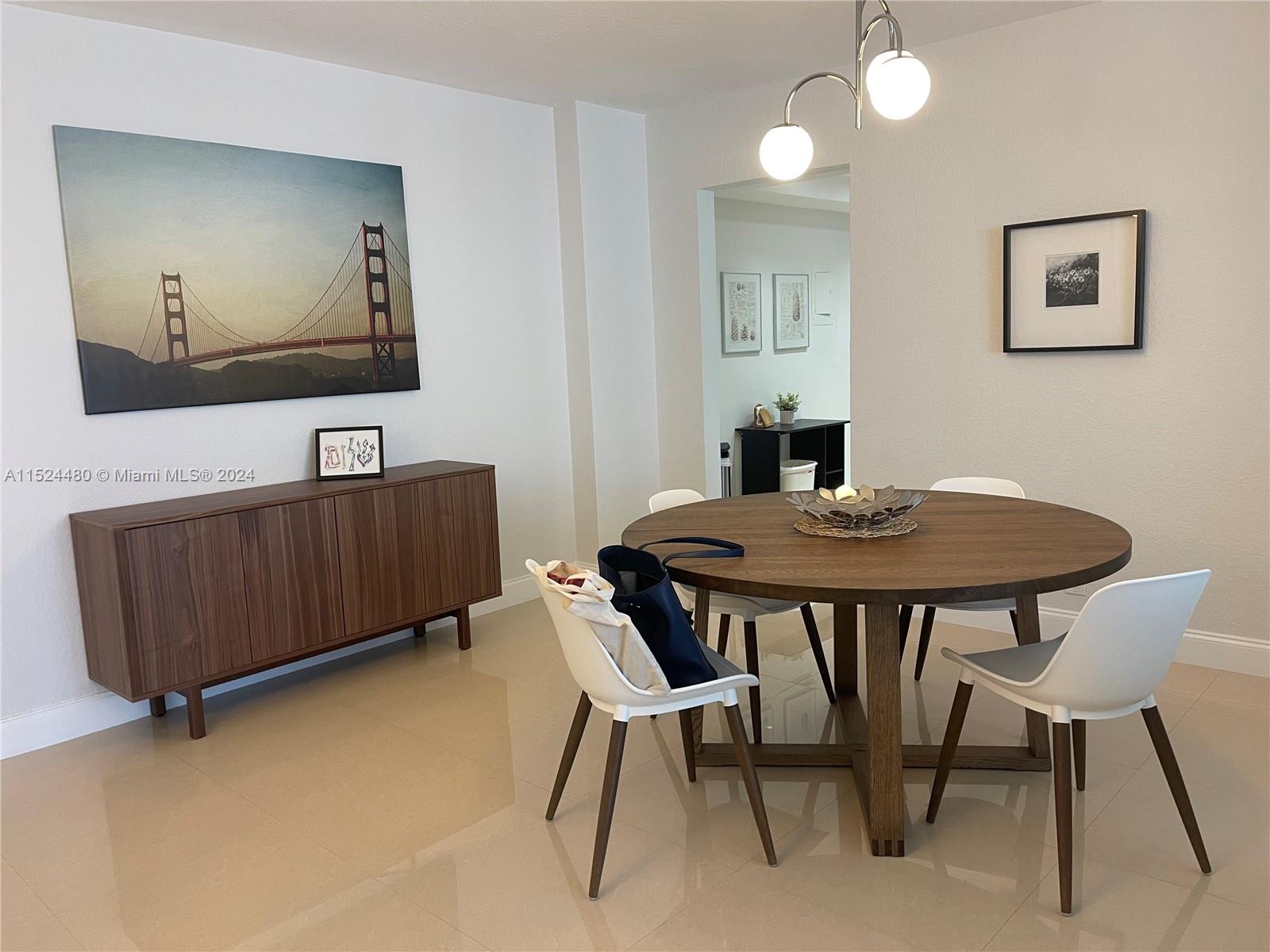 A dining room features a round wooden table, white chairs, and a large bridge painting — 3801 S OCEAN DR # 15V, Hollywood FL 33019, HOLLYWOOD, FL