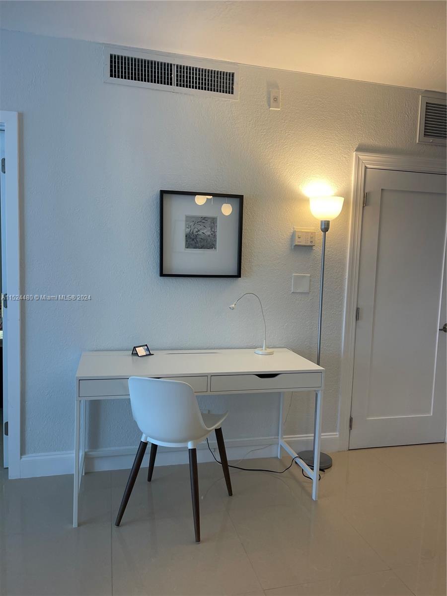 A white desk and chair sit against a wall with a lamp and artwork — 3801 S OCEAN DR # 15V, Hollywood FL 33019, HOLLYWOOD, FL