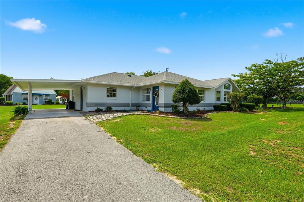 A single-story house with a white exterior, a blue front door, and an attached carport — 6935 NW HIGHWAY 225A, OCALA, FL