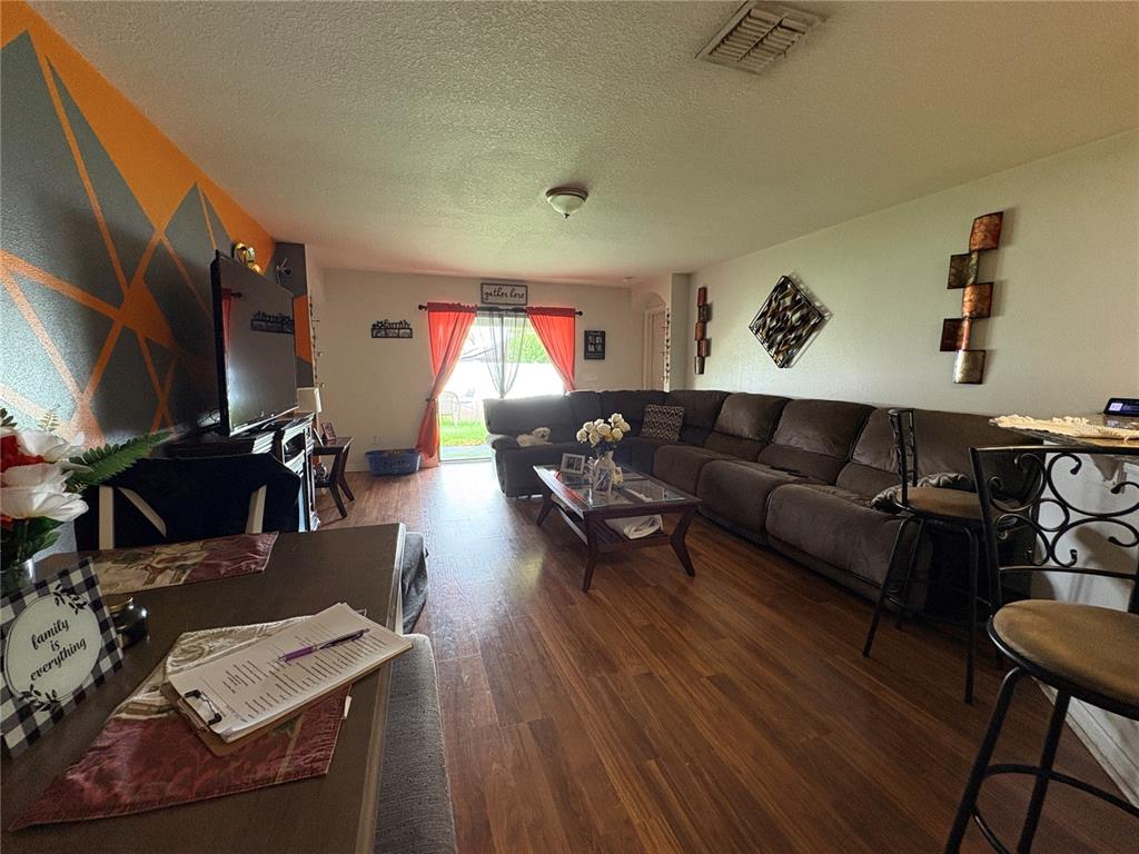 A living room features wood-look flooring, a large sectional sofa, and a geometric accent wall — 14217 ALISTAR MANOR DRIVE, WIMAUMA, FL