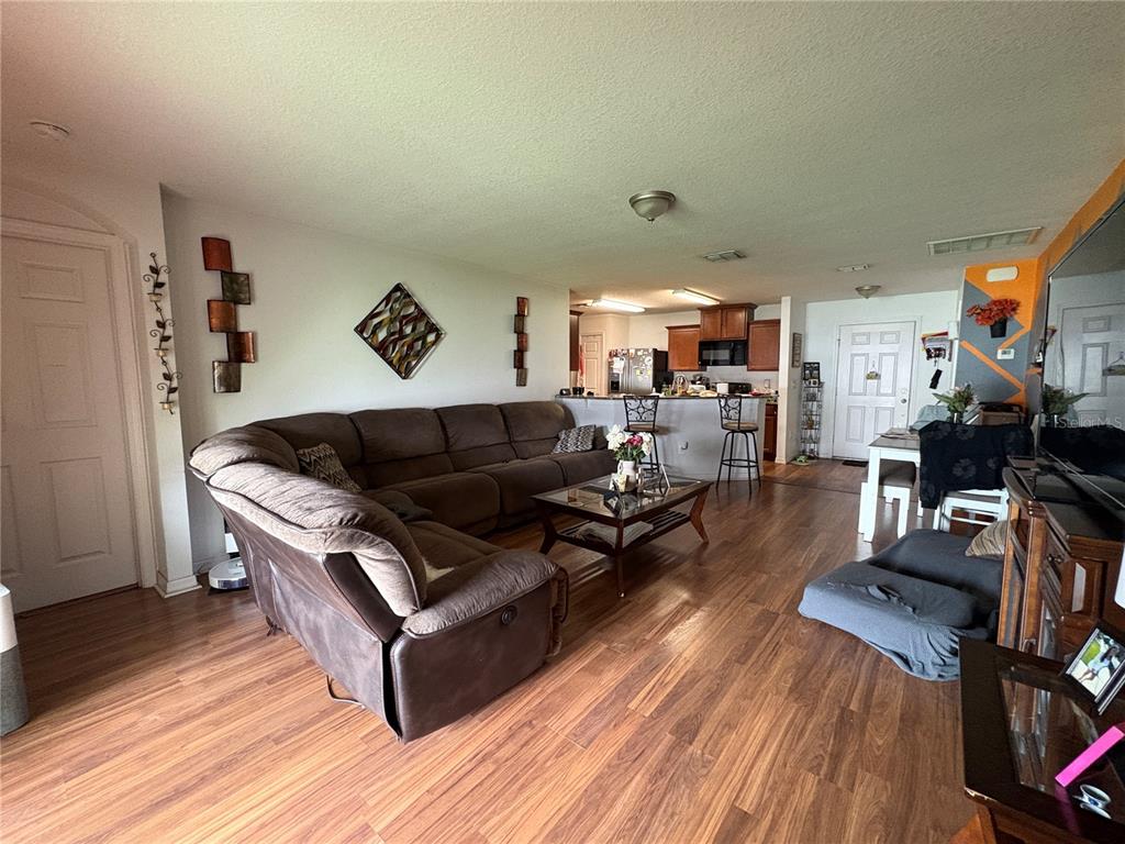 A living room with wood-look flooring, a large brown sectional sofa, and an open kitchen — 14217 ALISTAR MANOR DRIVE, WIMAUMA, FL