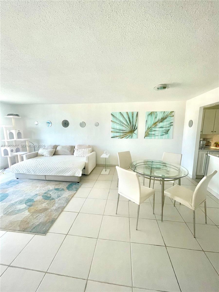 This living and dining area features white tile flooring, a sofa bed, and a glass table — 1817 S Ocean Dr # 219, Hallandale Beach FL 33009, HALLANDALE BEACH, FL