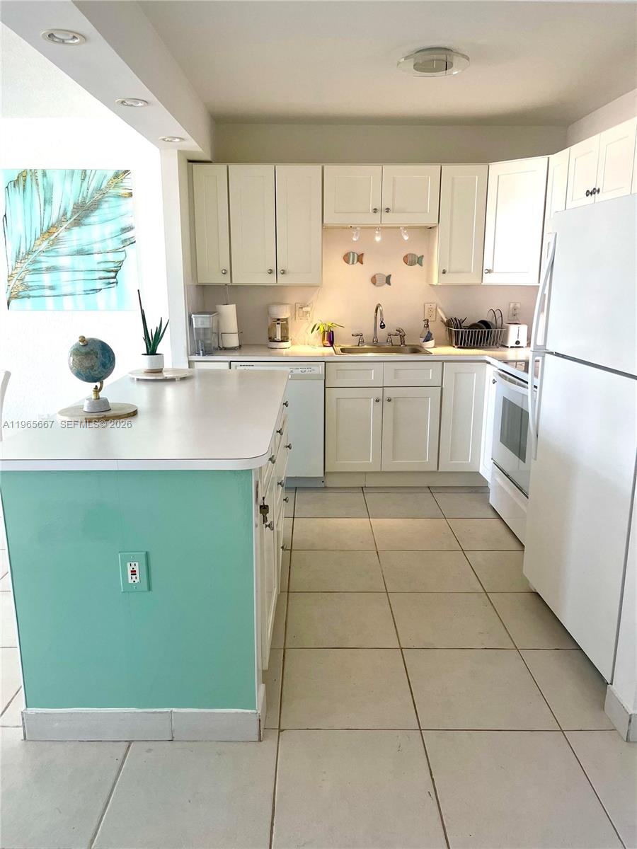 A kitchen features white cabinets, a teal island, and light-colored tile flooring — 1817 S Ocean Dr # 219, Hallandale Beach FL 33009, HALLANDALE BEACH, FL