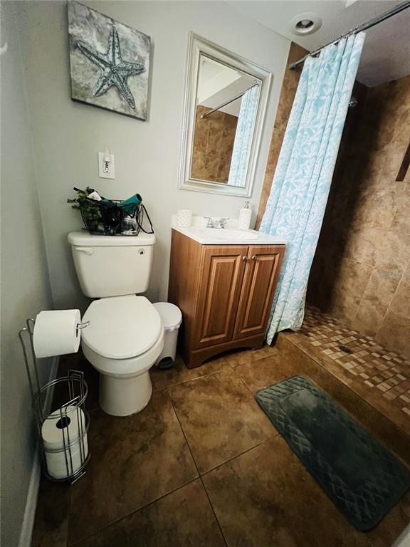 A bathroom features a toilet, a wooden vanity, a shower with a curtain, and tile flooring — 7705 ILEX DRIVE, PORT RICHEY, FL