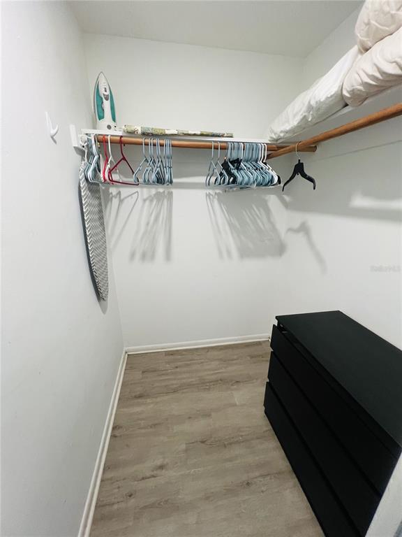 A walk-in closet features light wood-look flooring, a black dresser, and a hanging rod — 7705 ILEX DRIVE, PORT RICHEY, FL