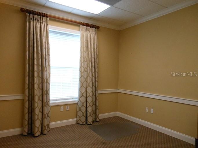 An empty office room features beige walls, a window with patterned curtains, and carpeted flooring — 1740 SE 18TH STREET UNIT 901, OCALA, FL