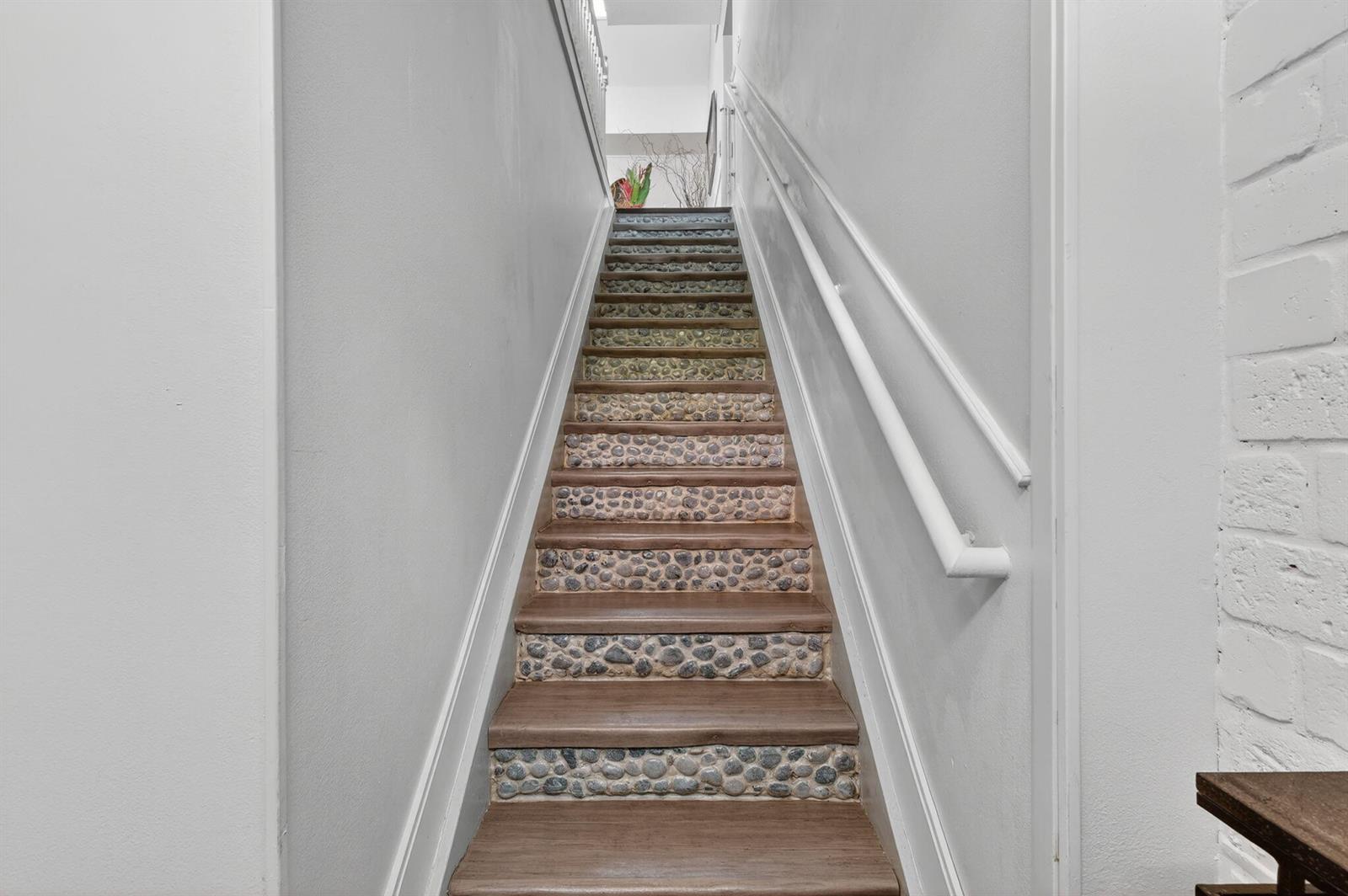 A staircase features wooden treads and risers decorated with embedded river stones between white walls — 1679 SE Pomeroy Street # 1, Stuart FL 34997, STUART, FL