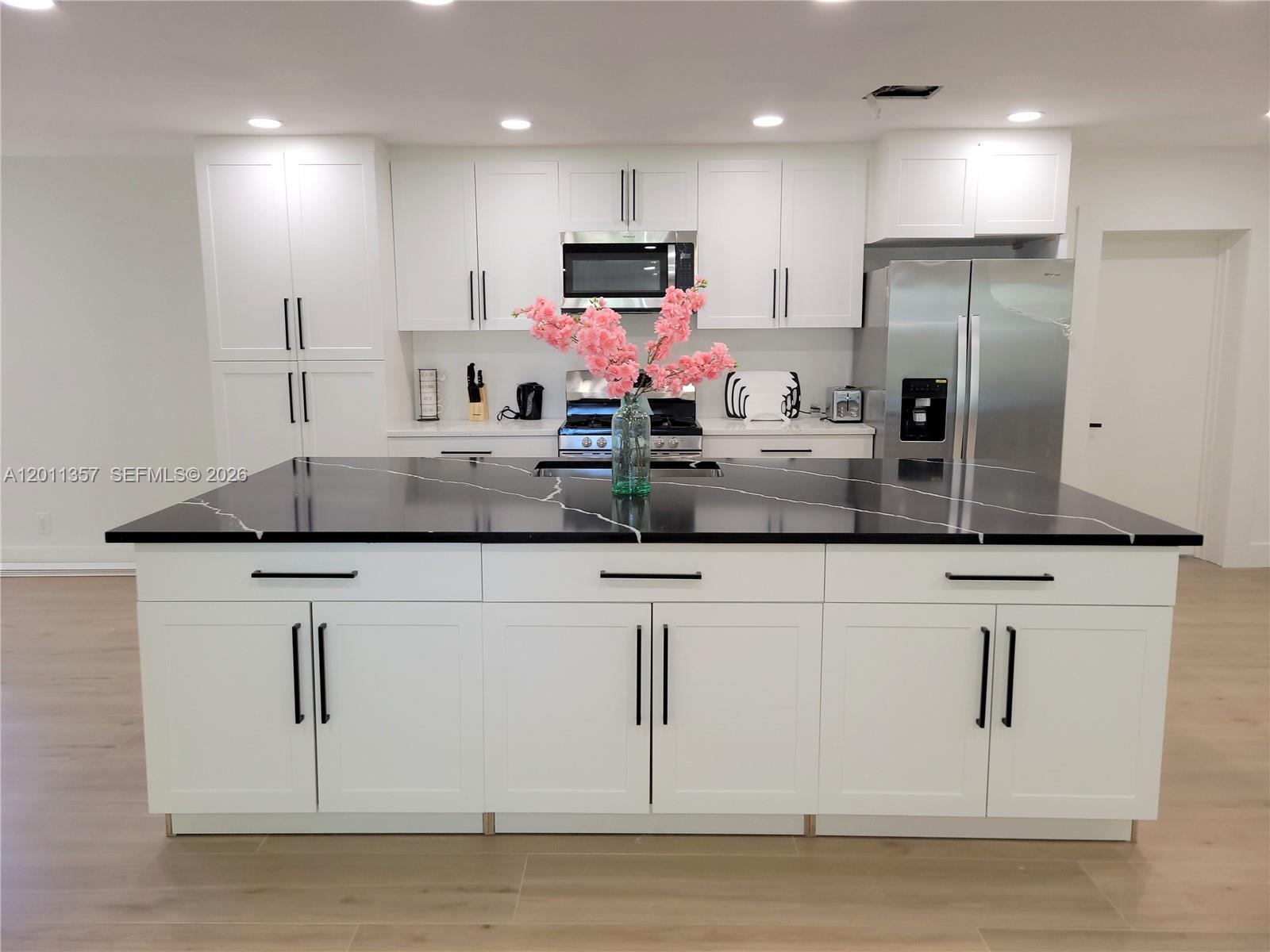 A modern kitchen features white cabinets, a large black island with white veining, and stainless appliances — 735 Tradewind Dr, North Palm Beach FL 33408, NORTH PALM BEACH, FL