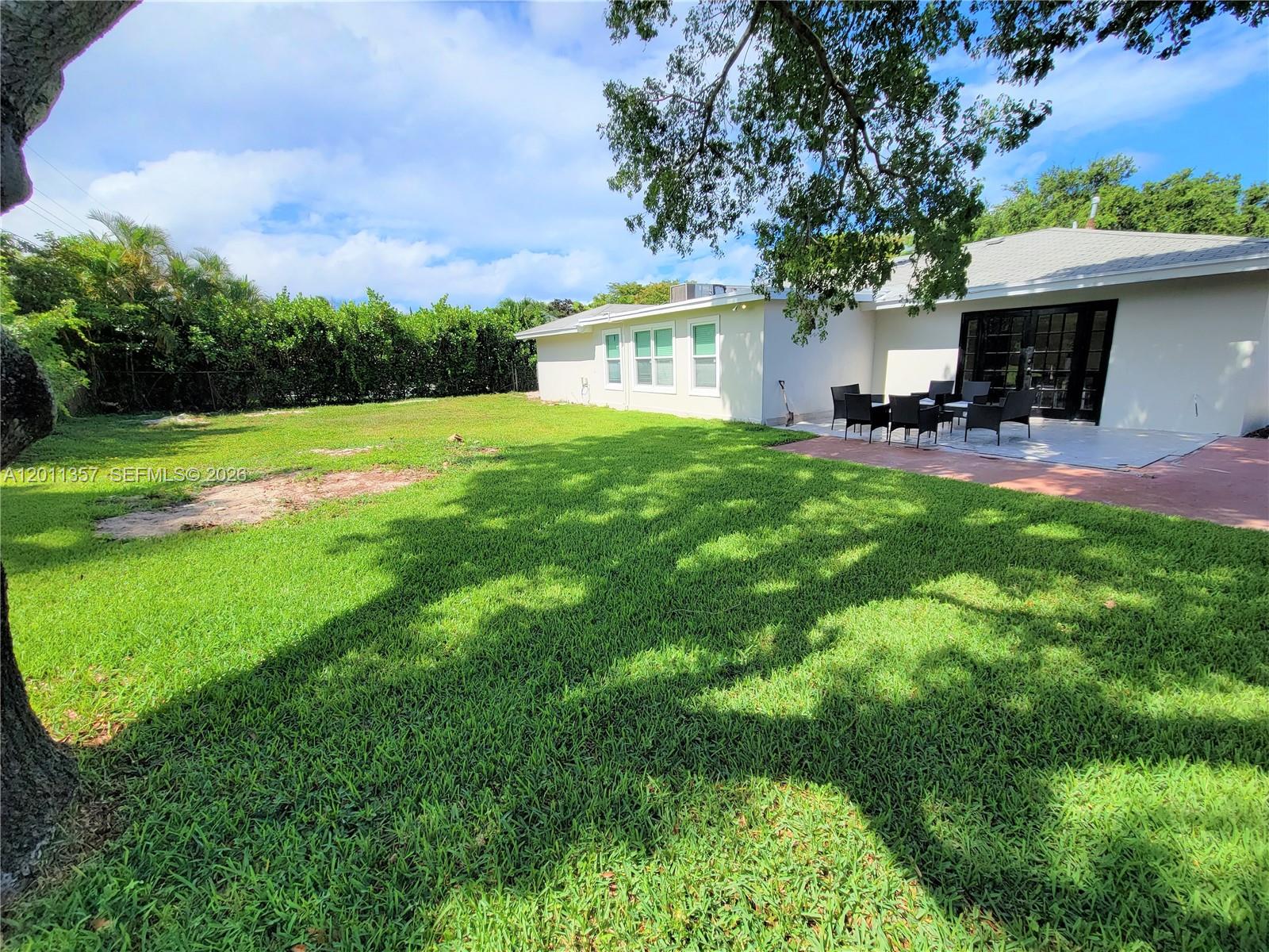 A grassy backyard features a patio with outdoor furniture and a large shade tree — 735 Tradewind Dr, North Palm Beach FL 33408, NORTH PALM BEACH, FL