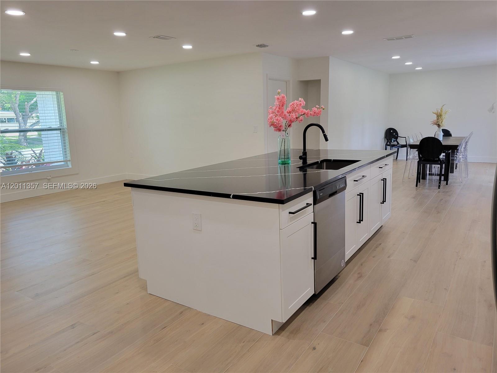 A kitchen island with a black countertop and white cabinets sits in an open-concept room — 735 Tradewind Dr, North Palm Beach FL 33408, NORTH PALM BEACH, FL