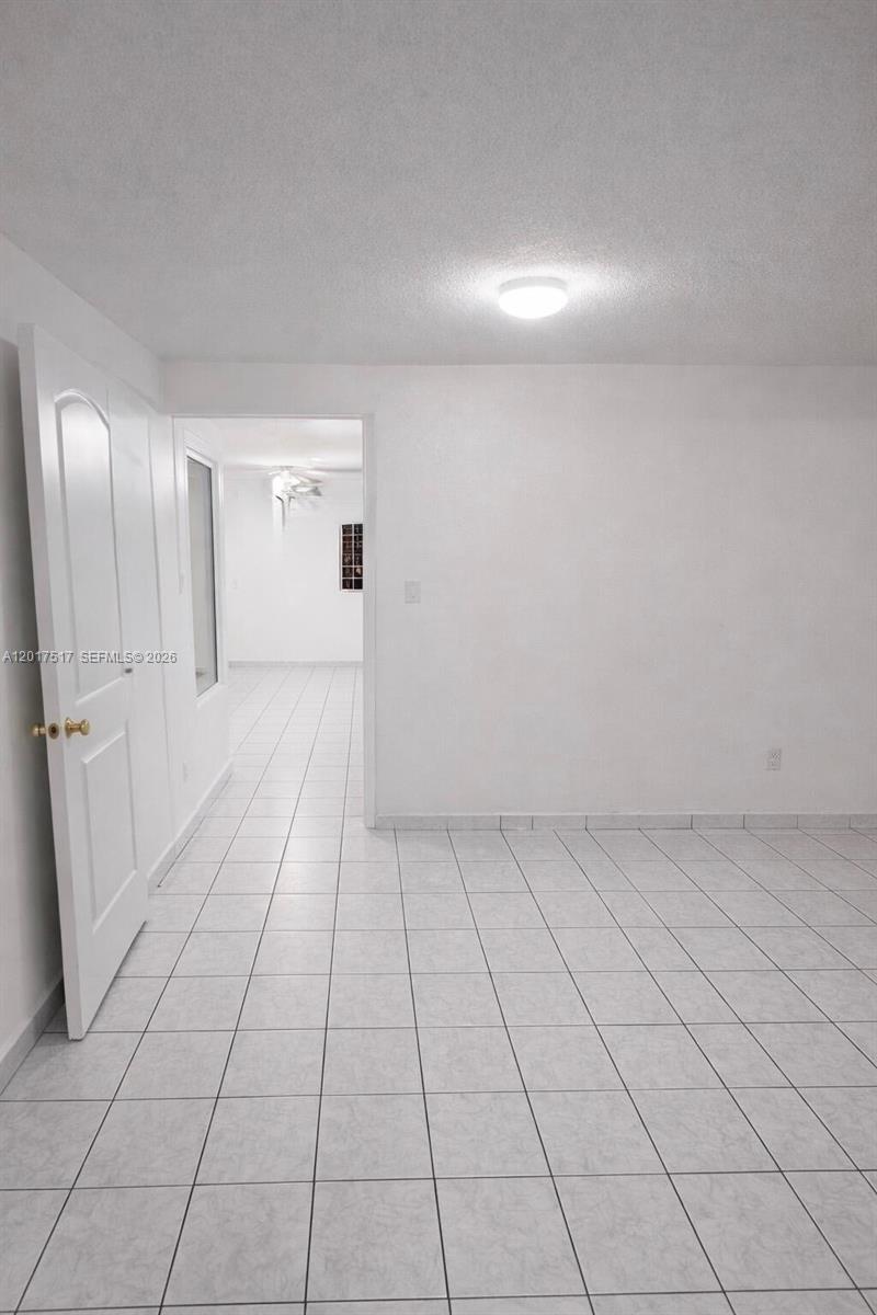 A room with white walls and light-colored tiled flooring leads into an adjacent space — 538 E 13th St, Hialeah FL 33010, HIALEAH, FL