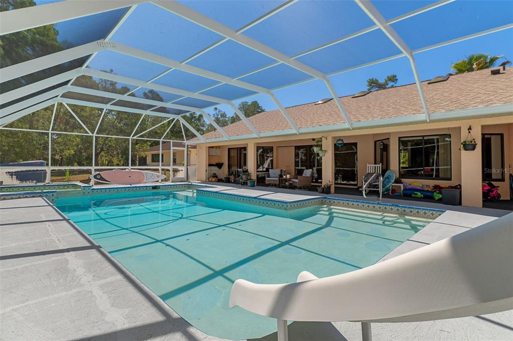 A screened-in swimming pool with a slide and a covered patio area — 8959 NAKOMA WAY, WEEKI WACHEE, FL