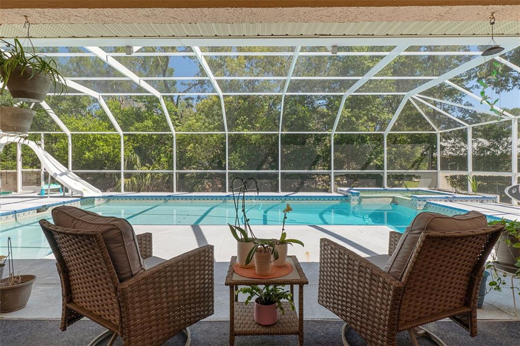 A covered patio with wicker chairs overlooks a swimming pool enclosed by a screen cage — 8959 NAKOMA WAY, WEEKI WACHEE, FL