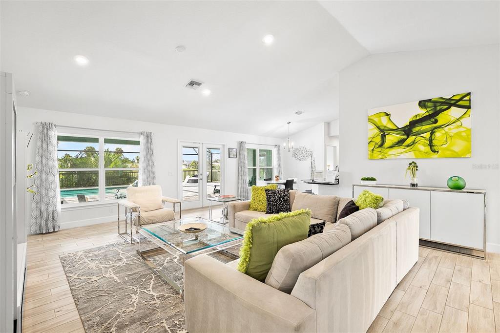 A bright living room features a beige sectional, glass coffee table, and views of a pool — 240 CADDY ROAD, ROTONDA WEST, FL