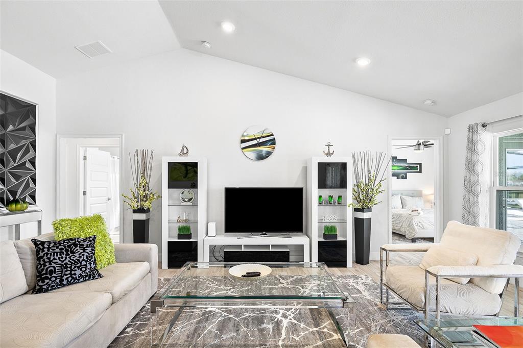 A living room features a vaulted ceiling, white walls, a television console, and modern furniture — 240 CADDY ROAD, ROTONDA WEST, FL