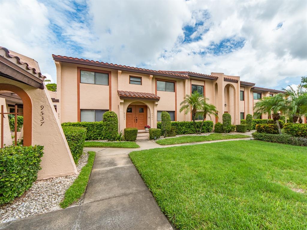A two-story stucco apartment building features a tan exterior, tile roof, and landscaped front lawn — 9543 86TH AVENUE UNIT 9543, SEMINOLE, FL