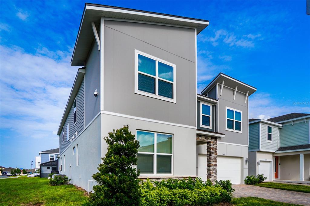 A two-story gray house with a stone-accented garage and a paved driveway — 2341 SALTY WINDS WAY, KISSIMMEE, FL