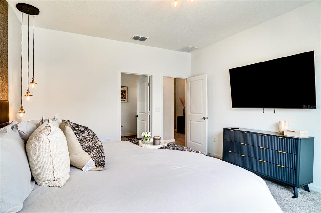 A bedroom features a bed with decorative pillows, a dark blue dresser, and a wall-mounted television — 2341 SALTY WINDS WAY, KISSIMMEE, FL