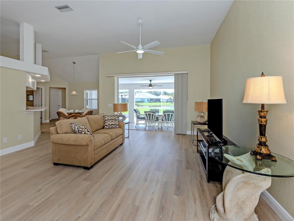 A living room with light wood floors, a tan sofa, and a view of a patio — 5078 WINTER ROSE WAY, VENICE, FL