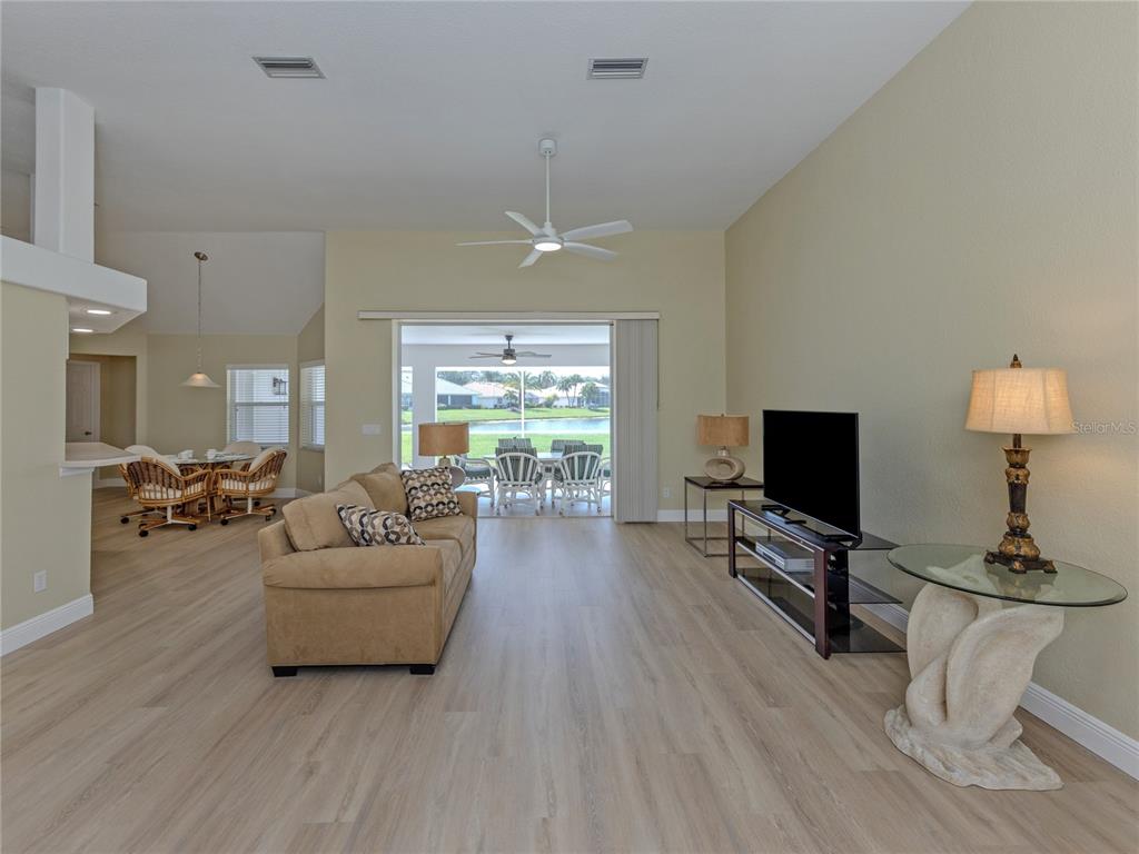A living room features light wood-look flooring, a beige sofa, a television, and sliding glass doors — 5078 WINTER ROSE WAY, VENICE, FL