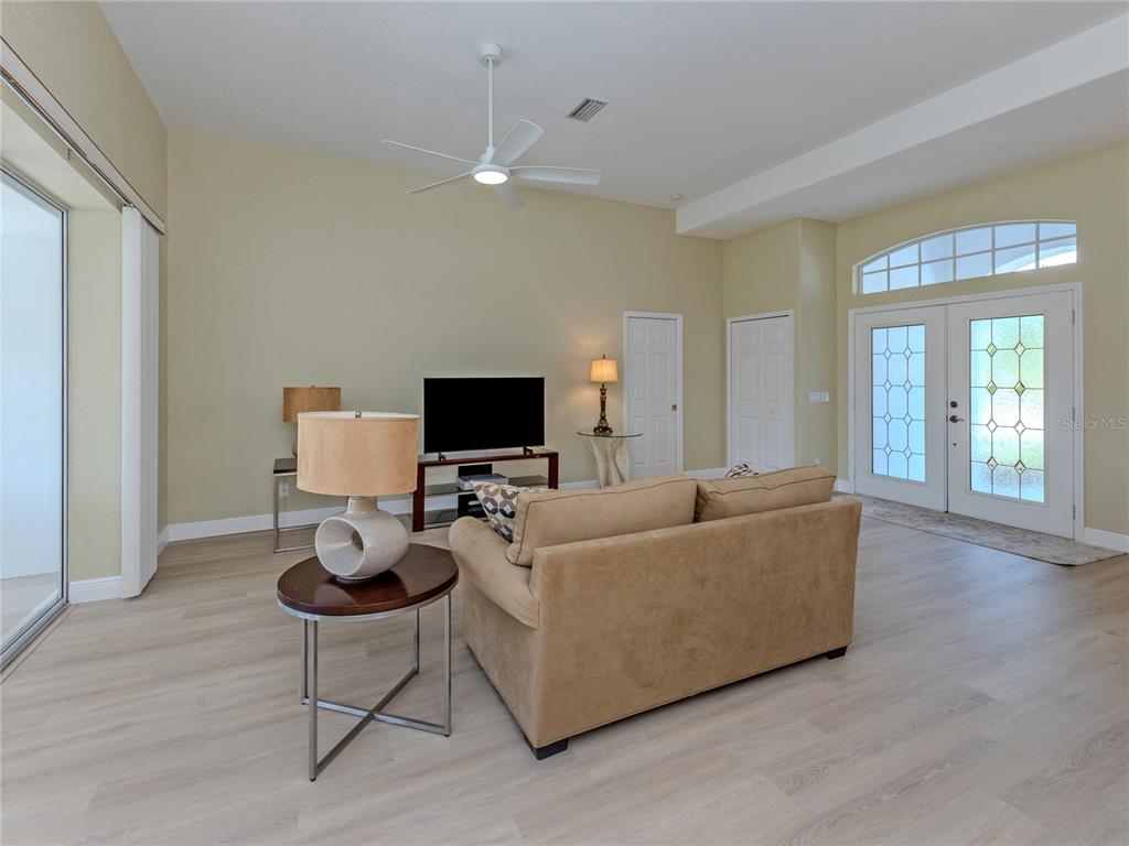A living room features light wood-look flooring, a tan sofa, a ceiling fan, and double doors — 5078 WINTER ROSE WAY, VENICE, FL