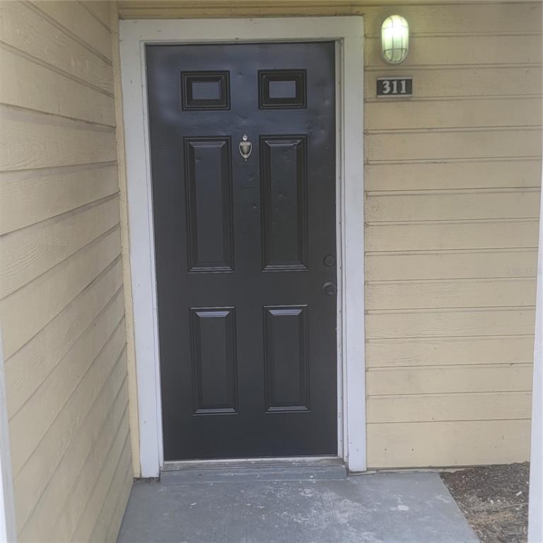 A dark brown front door with a door knocker is set in a beige-sided exterior — 1089 S HIAWASSEE ROAD UNIT 311, ORLANDO, FL