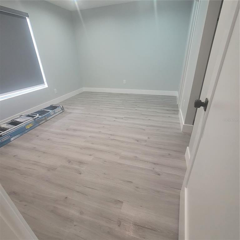 An empty room features light gray walls, white baseboards, and wood-look laminate flooring — 1089 S HIAWASSEE ROAD UNIT 311, ORLANDO, FL