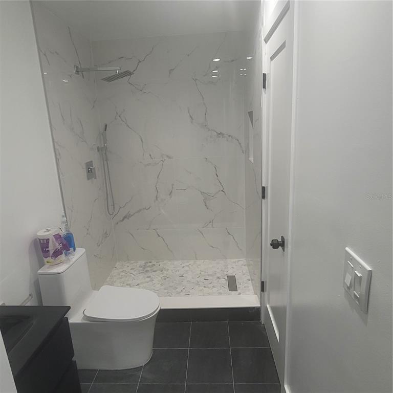 A bathroom features a walk-in shower with marble-look tile, a toilet, and dark floor tiles — 1089 S HIAWASSEE ROAD UNIT 311, ORLANDO, FL