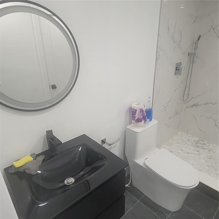 A modern bathroom features a black vanity, a round mirror, and a marble-tiled walk-in shower — 1089 S HIAWASSEE ROAD UNIT 311, ORLANDO, FL