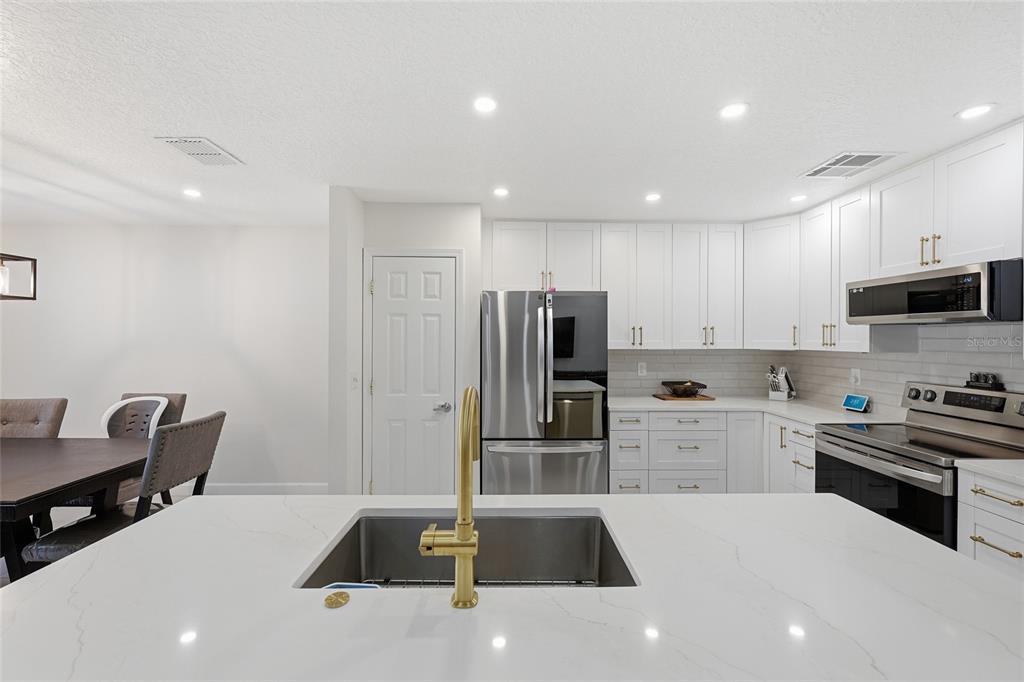 A modern kitchen features white cabinetry, stainless steel appliances, and a central quartz-topped island — 10251 TREVOR CREEK DRIVE W, JACKSONVILLE, FL