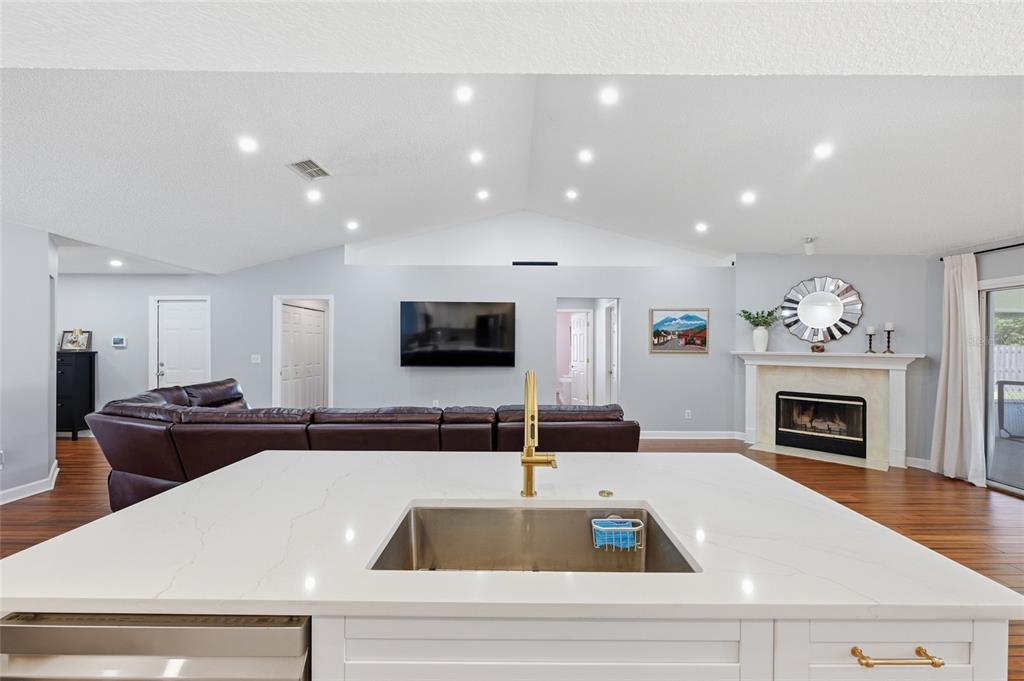 A kitchen island with a white countertop and gold faucet overlooks a living room area — 10251 TREVOR CREEK DRIVE W, JACKSONVILLE, FL