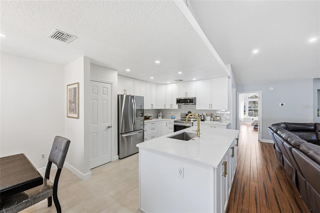 A modern kitchen features white cabinetry, stainless steel appliances, a quartz island, and wood flooring — 10251 TREVOR CREEK DRIVE W, JACKSONVILLE, FL