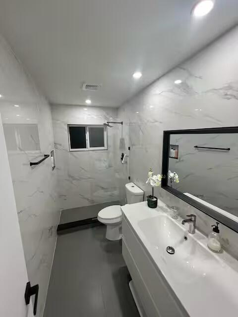 A modern bathroom features white marble-patterned walls, a gray floor, and a white vanity — 739 SE 12th Avenue, Deerfield Beach FL 33441, DEERFIELD BEACH, FL
