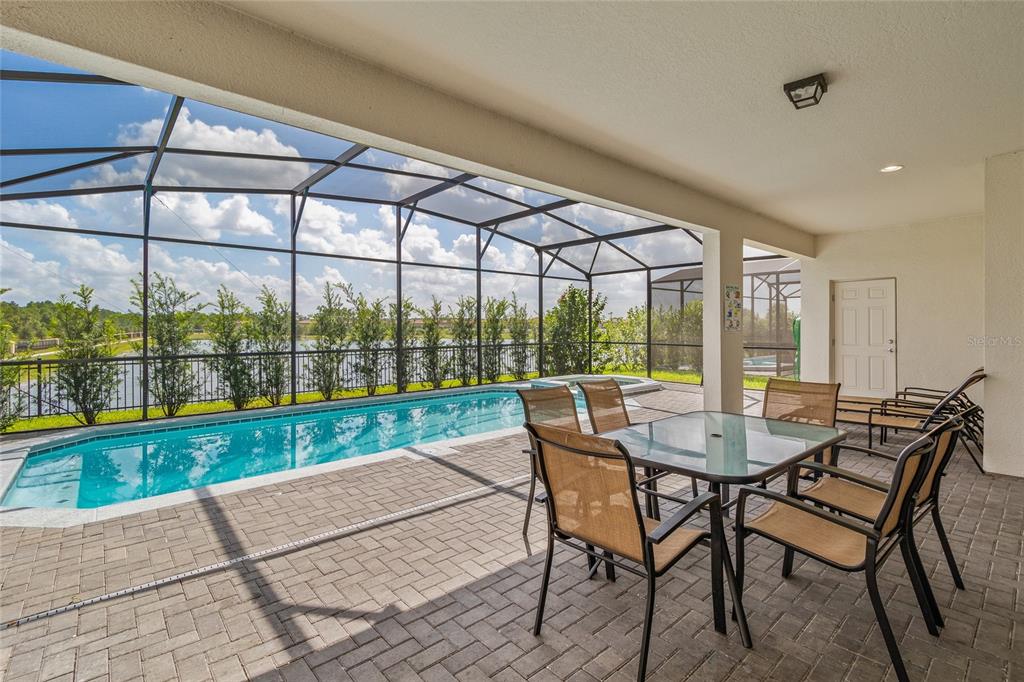 A covered patio features a dining set, a screened-in pool, and a view of a lake — 2451 LUXOR DRIVE, KISSIMMEE, FL