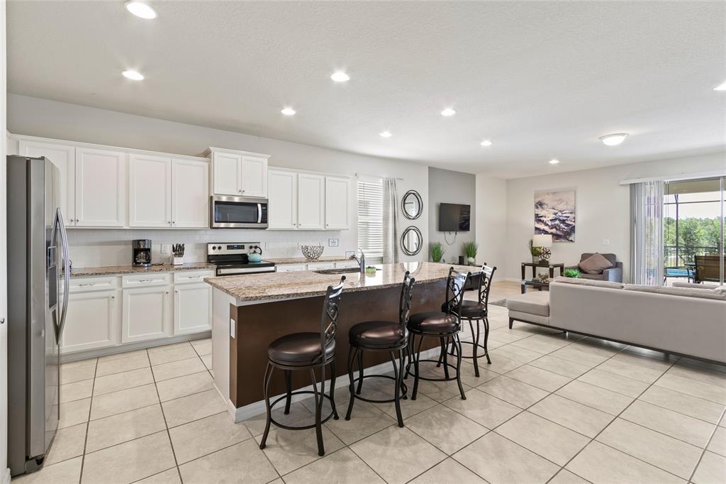 A kitchen with white cabinets and granite countertops opens into a living room with tile floors — 2451 LUXOR DRIVE, KISSIMMEE, FL