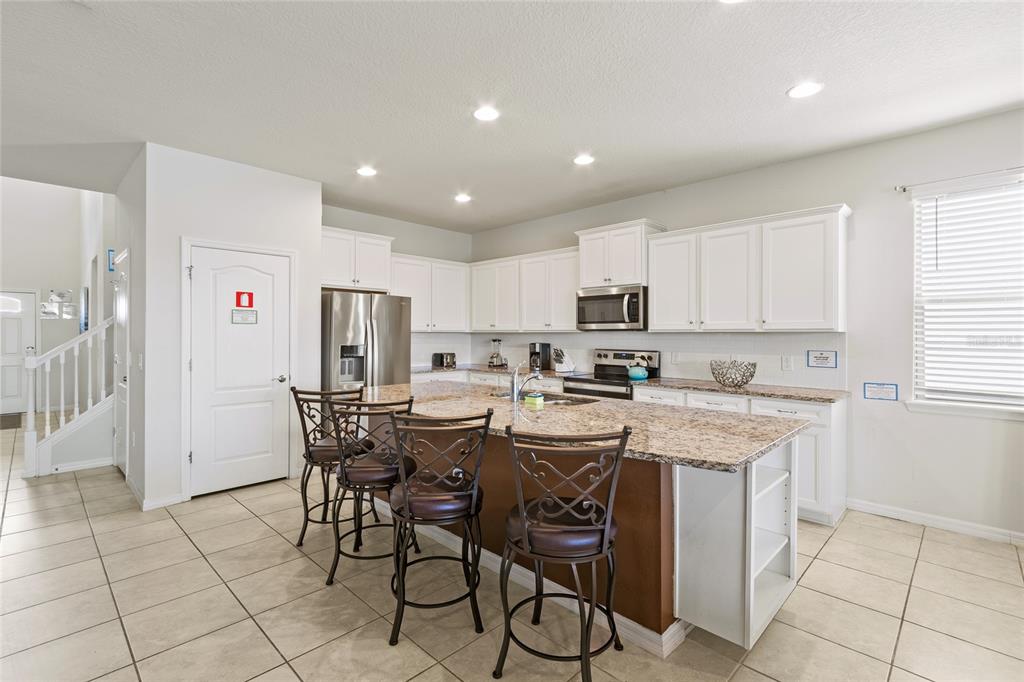 A kitchen features white cabinets, granite countertops, a center island with bar stools, and tile flooring — 2451 LUXOR DRIVE, KISSIMMEE, FL