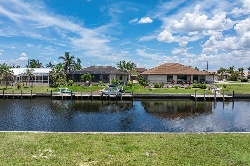 A canal-front view of residential houses with boat docks and palm trees under a blue sky — 1237 WHIPPOORWILL COURT, PUNTA GORDA, FL