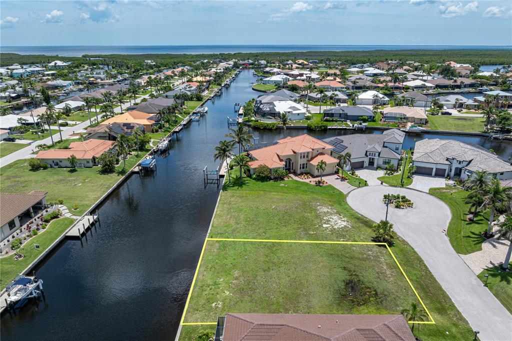 An aerial view shows a vacant waterfront residential lot outlined in yellow near a canal — 1237 WHIPPOORWILL COURT, PUNTA GORDA, FL