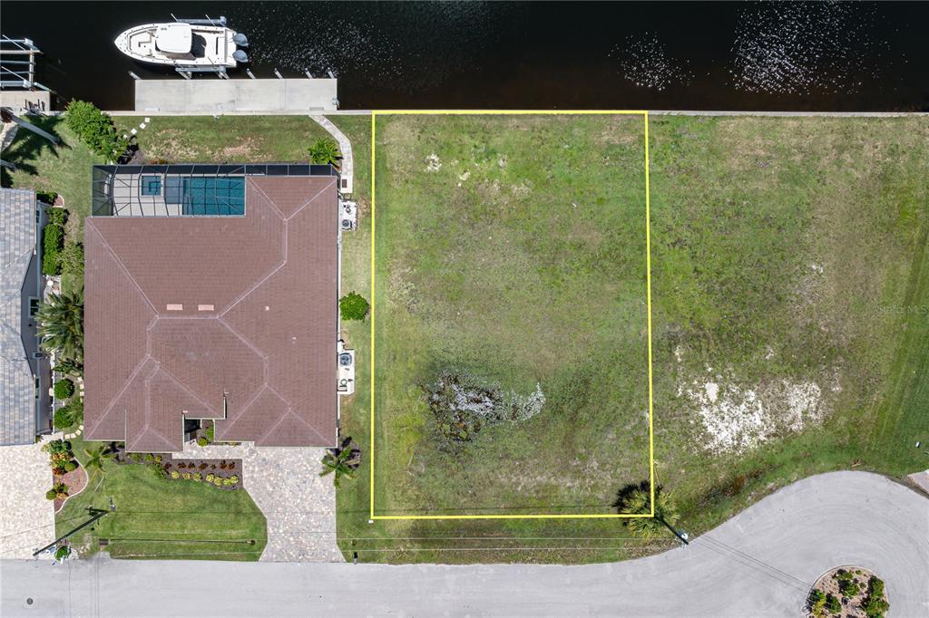 An aerial view shows a vacant waterfront lot outlined in yellow next to a house — 1237 WHIPPOORWILL COURT, PUNTA GORDA, FL
