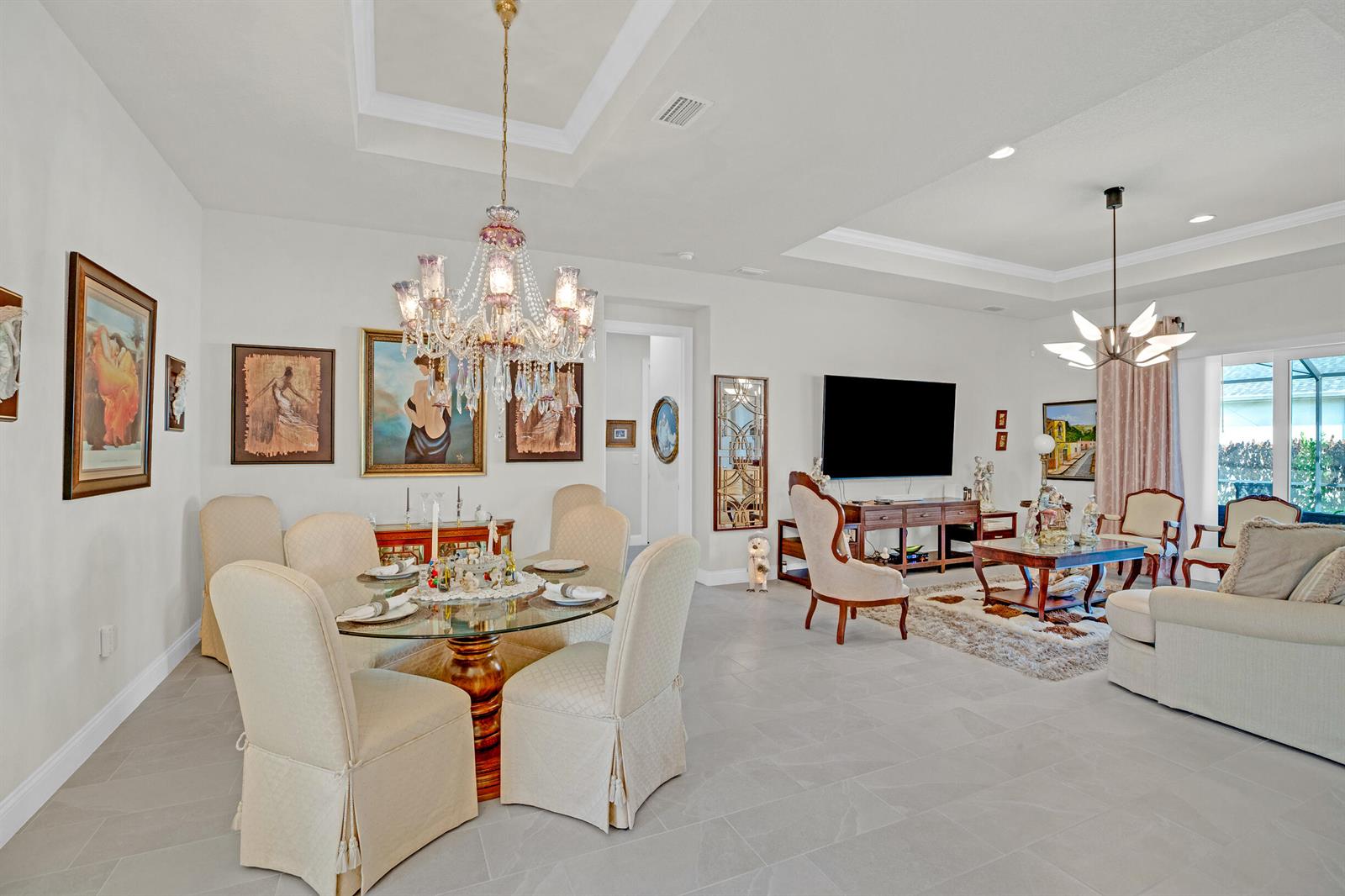 An open-concept dining and living area features a glass table, chandelier, and neutral furniture — 4160 Negal Circle, Melbourne FL 32901, MELBOURNE, FL