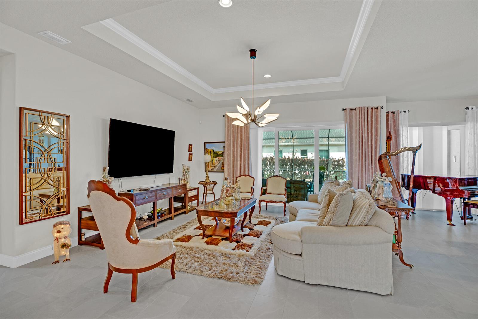A living room features a tray ceiling, a chandelier, a television, and a grand piano — 4160 Negal Circle, Melbourne FL 32901, MELBOURNE, FL