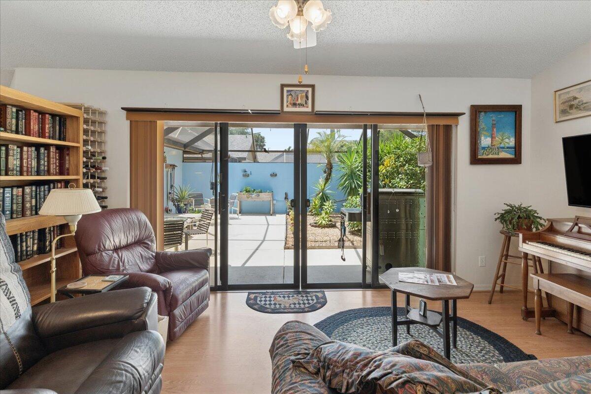 A living room features a bookshelf, leather chairs, a piano, and sliding doors to a patio — 6287 N Mirror Lake Drive, Sebastian FL 32958, SEBASTIAN, FL