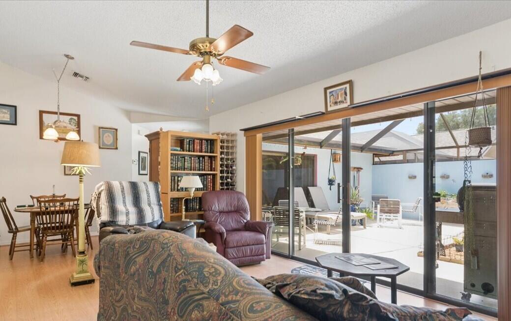 A living room with a ceiling fan, wooden bookcase, and sliding glass doors to a patio — 6287 N Mirror Lake Drive, Sebastian FL 32958, SEBASTIAN, FL